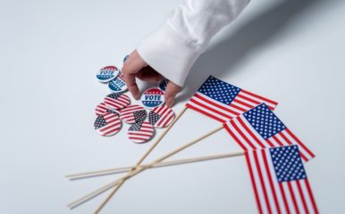 An arm grabbing a "vote" pin on a table full of American flag pins and flags.